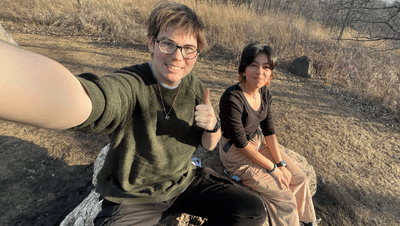 Felix and his friend sit on a rock in the sun, giving a thumbs up
